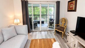 A living room with a sofa, a chair, a television, a wooden coffee table, and a sliding glass door leading to an outdoor area with furniture. - Renovated Condo Across from Siesta Key Beach | Heated Pool | Dogs Welcome (Siesta Key)