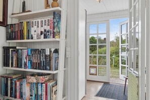 A room with a bookshelf filled with books, a door leading outside, and a window with a view of greenery.