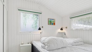 Une chambre à coucher avec un lit, deux lampes fixées au mur, un radiateur et une fenêtre donnant sur un paysage verdoyant.