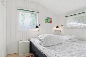 A bedroom with a bed, two wall-mounted lamps, a radiator, and a window with a view of greenery. - Cozy house by Klitgård Fishing Village (Nibe)