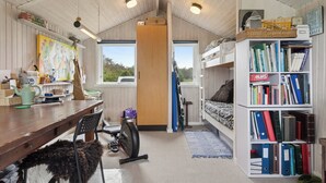 Une pièce de taille modeste avec un plafond en bois, un bureau avec une chaise, une bibliothèque, un lit superposé et une fenêtre.
