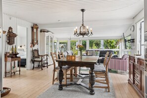 A dining area with a wooden table and chairs, a chandelier, and a view of the outdoors. - Cozy house by Klitgård Fishing Village (Nibe)
