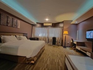 A hotel room with a large bed, a desk, a chair, a television, and a curtain. - OYO 1178 Plaza Hotel Tanjung Pinang (Tanjung Pinang)