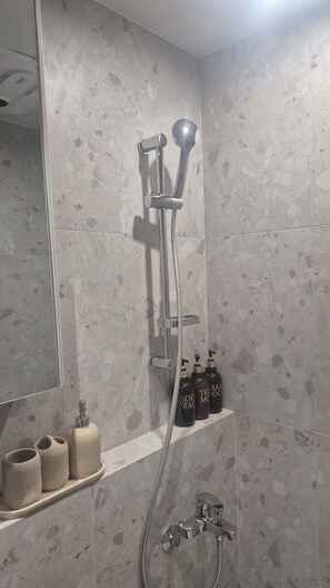Ein Badezimmer mit Dusche, Spiegel und Ablage für Pflegeprodukte.