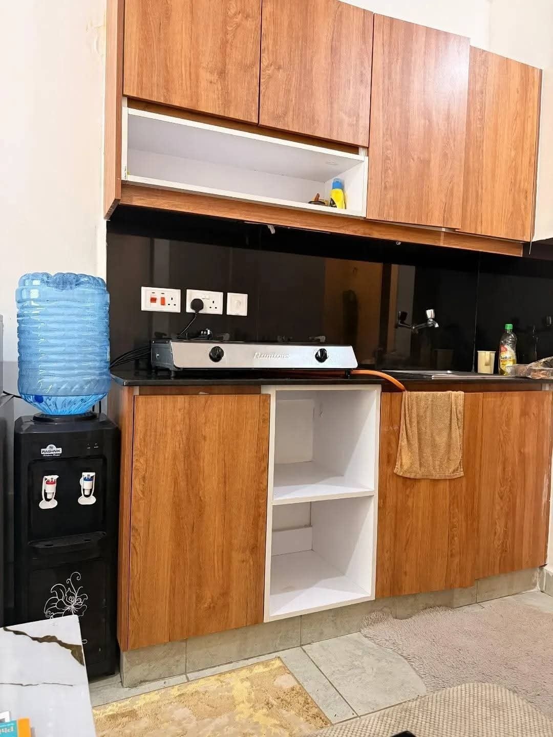 A kitchen with wooden cabinets, a gas stove, a water dispenser, and a towel hanging on the counter.
