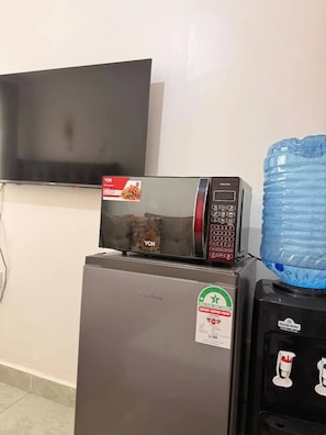 Ein Kühlschrank mit einer Mikrowelle darüber, ein Wasserspender und ein an der Wand befestigter Fernseher.