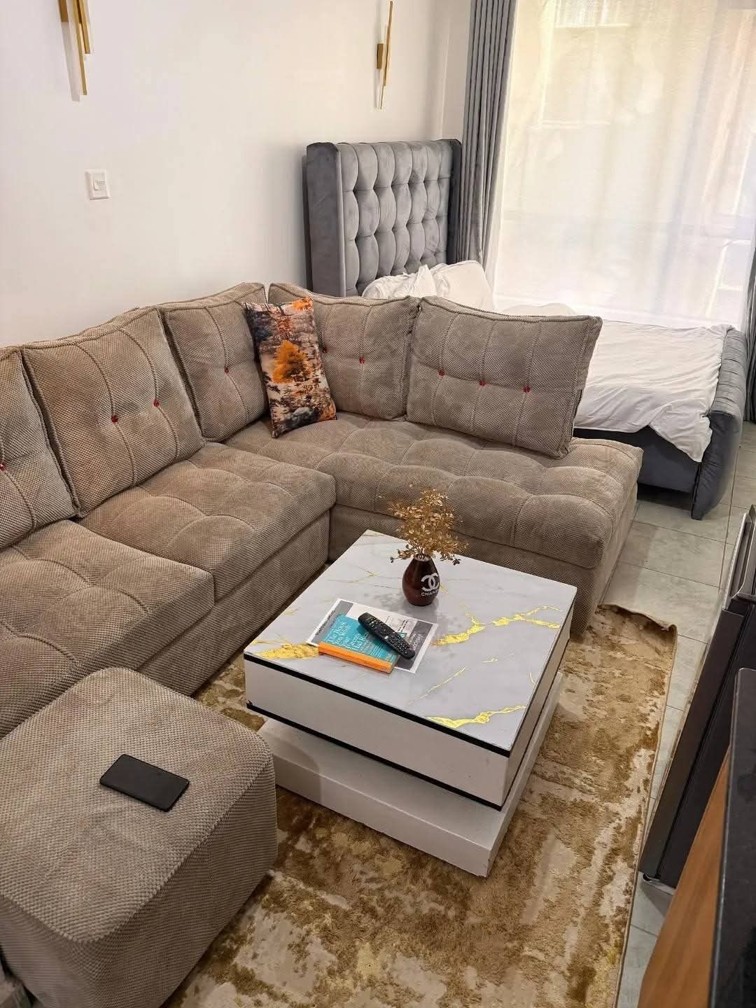 A modern living room with a sectional sofa, a coffee table, and a grey tufted headboard.
