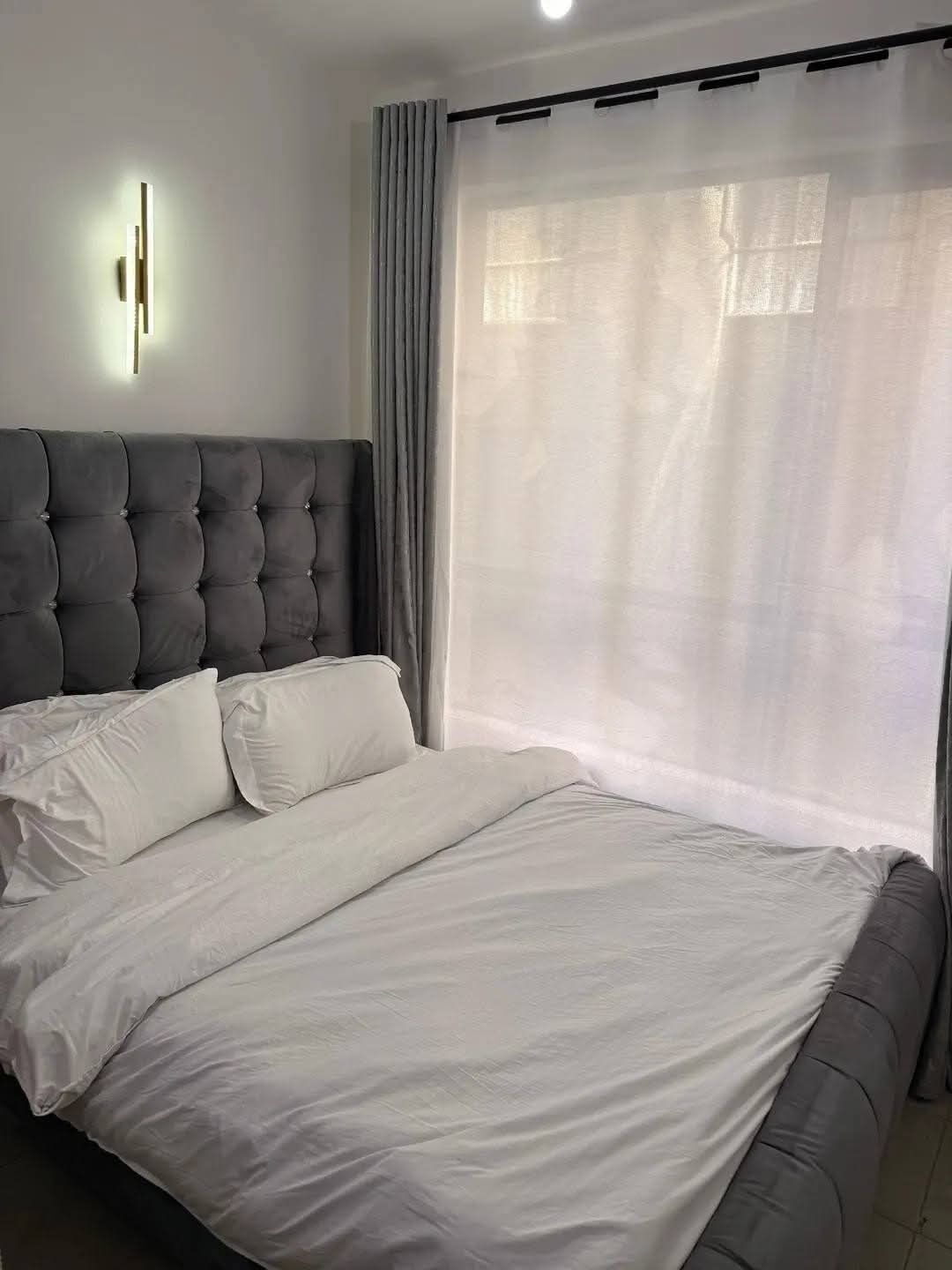 Un dormitorio con una cama grande, cabecera y una ventana con cortinas traslúcidas.
