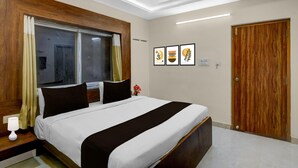 A hotel room with a bed, wooden headboard, a window with curtains, a bedside table with a lamp, and a door. - Premium Financial District Gachibowli Srinika (Hyderabad)