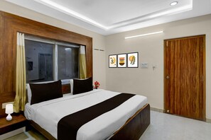Ein Hotelzimmer mit Bett, Holz-Kopfteil, einem Fenster mit Vorhängen, einem Nachttisch mit Lampe und einer Tür.
