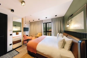 A hotel room with a large bed, a seating area with a chair and table, a view of the outdoors through the window, and a painting on the wall. - Hotel 21, Tbilisi (Tbilisi)