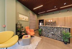A reception area with a wooden reception desk, a seating area with two chairs, and a wall-mounted shelf with plants. - Hotel 21, Tbilisi (Tbilisi)