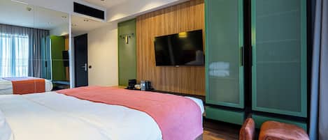 Una habitación de hotel moderna con una cama grande, un televisor de pantalla plana, un armario verde y una zona de estar con una pequeña mesa.