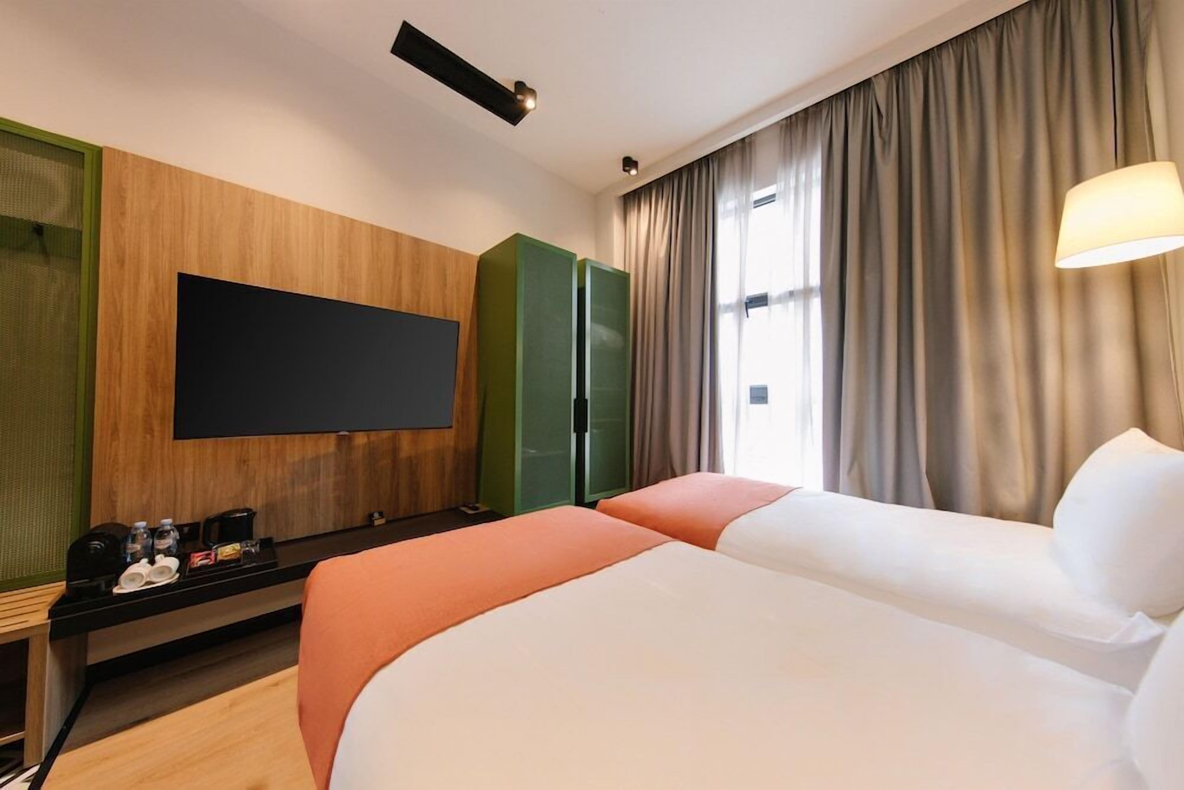 A hotel room with a flat-screen TV, a desk with a coffee maker, and two beds.