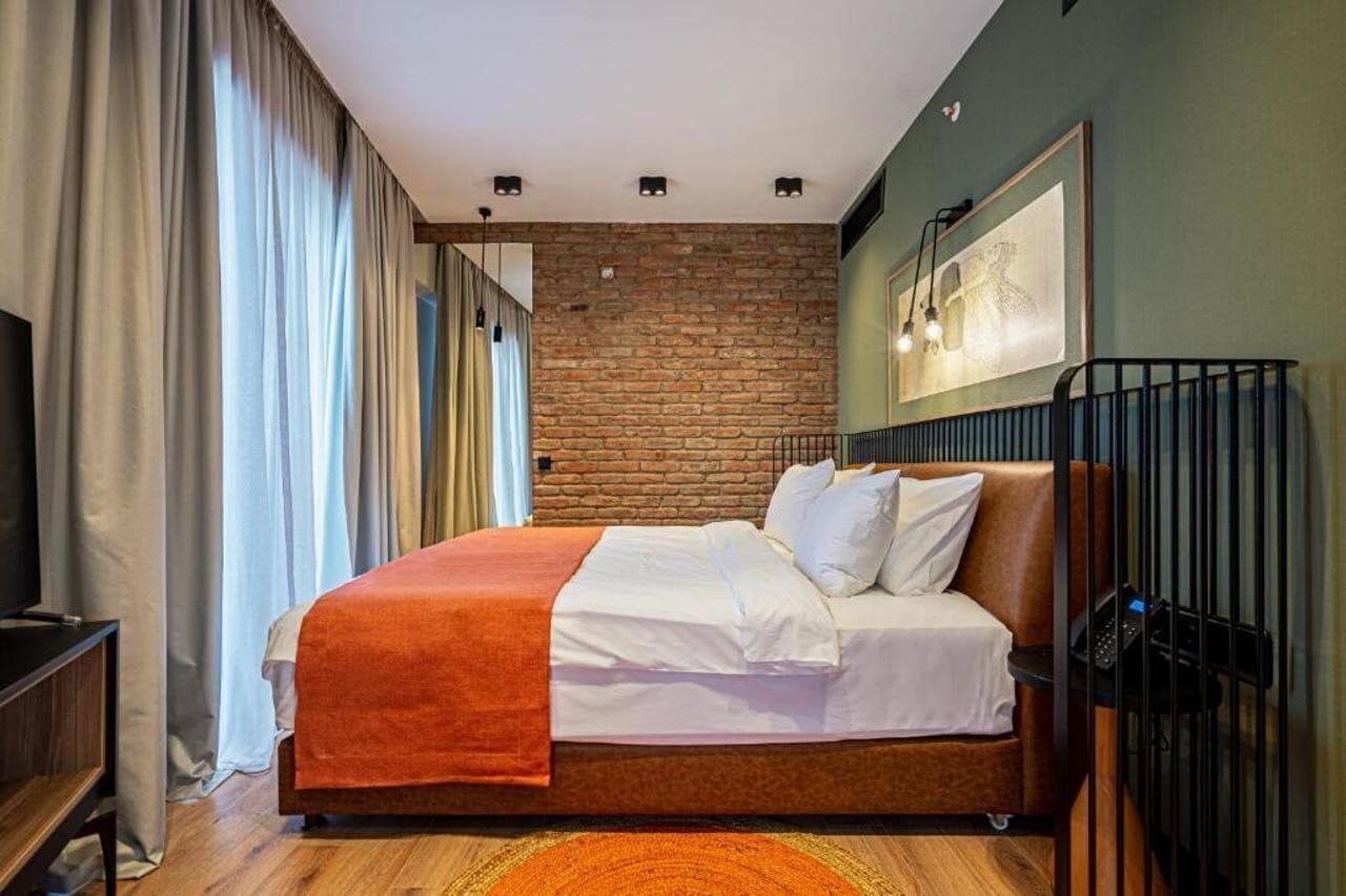 A bedroom with a brick wall, a bed with white bedding, a wooden floor, and a television on a stand.