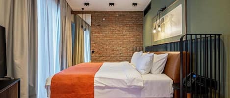 A bedroom with a brick wall, a bed with white bedding, a wooden floor, and a television on a stand.