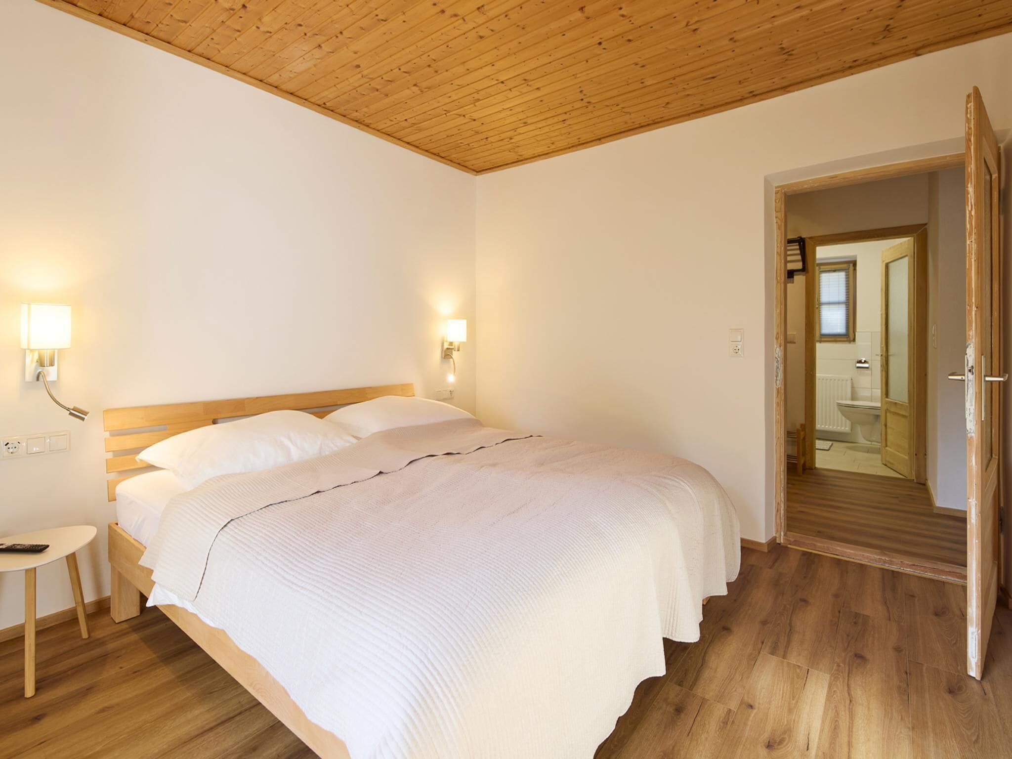 Ein Schlafzimmer mit Holzboden, einem Bett mit weißer Bettwäsche, Nachttischlampen und einem kleinen runden Tisch.