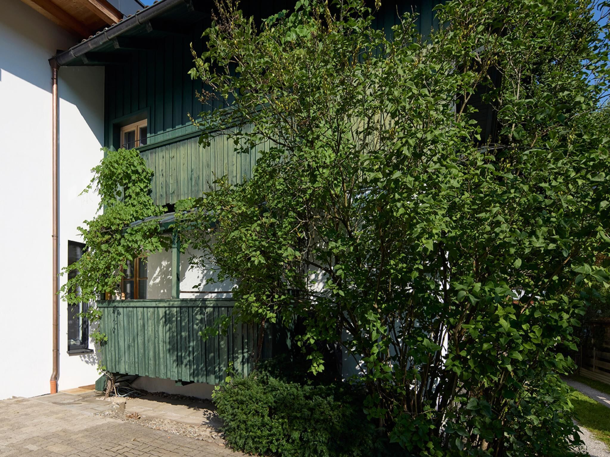 A two-story building with a green exterior, a visible balcony, and a tree in front.