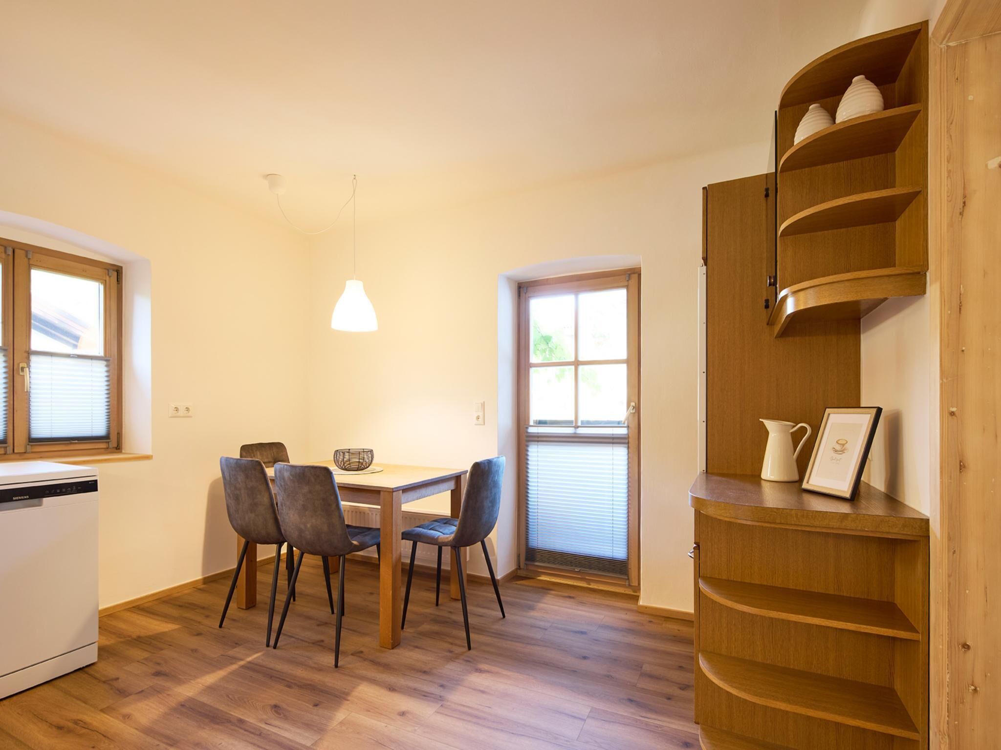 A compact kitchen with a dining area, a built-in wooden shelf unit, and a Siemens dishwasher.