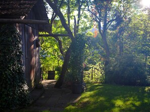 A garden pathway leading to a wooden structure with a sloped roof, surrounded by lush greenery and trees.