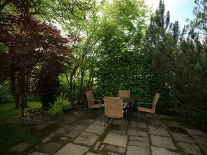 A stone patio with a table and chairs, surrounded by trees and greenery.
