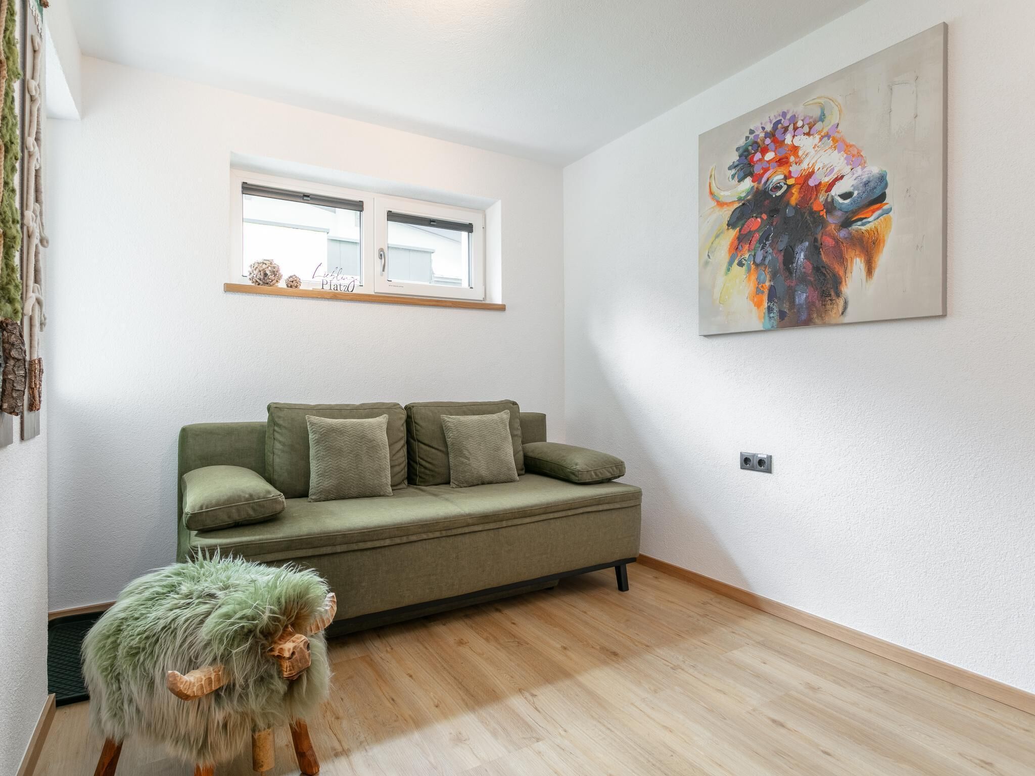 A modern living room with a green sofa, a fluffy green pouf, and a colorful abstract painting on the wall.