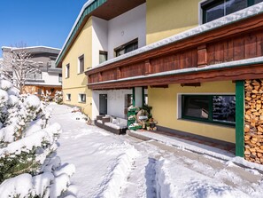 Un immeuble résidentiel recouvert de neige, doté d’une façade en bois, d’une entrée bien visible et d’un petit porche.