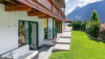 Et hotel med et overdækket udendørs opholdsområde, en velplejet græsplæne og et bjerg i baggrunden.