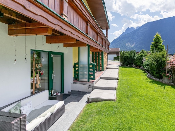 A hotel with a covered outdoor seating area, a well-maintained lawn, and a mountain backdrop.