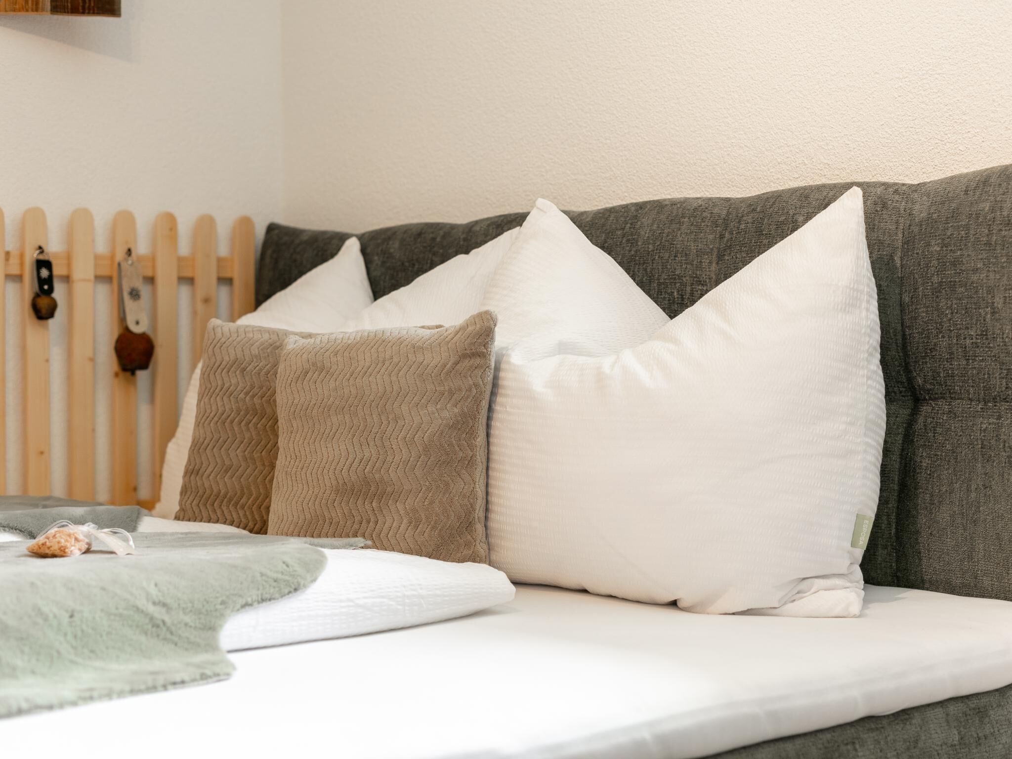 Ein Bett mit weißer Matratze, einer grauen Decke und mehreren Kissen in Weiß- und Beigetönen.