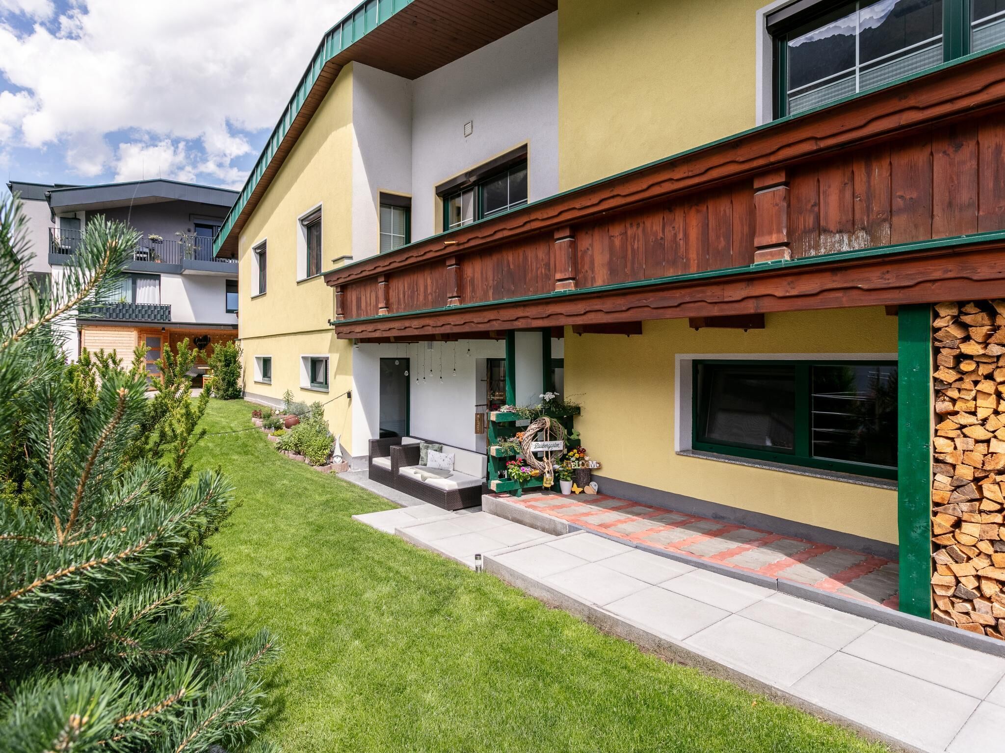 Ein mehrstöckiges Gebäude mit einem grünen Holzbalkon, einer Steinwand und einem gepflegten Rasen.