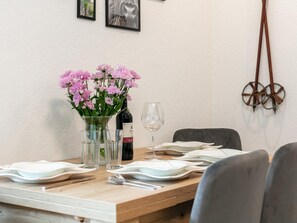 Une table à manger dressée avec des assiettes, des verres, une bouteille de vin et un vase de fleurs.