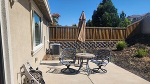 A patio with a table and chairs, a wooden fence, and a stone wall. - Fantastic 4-bedroom house with AC in cool Bay Point (Bay point)