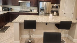 A kitchen with dark wood cabinets, granite countertops, stainless steel appliances, and a bar area with two stools. - Fantastic 4-bedroom house with AC in cool Bay Point (Bay point)