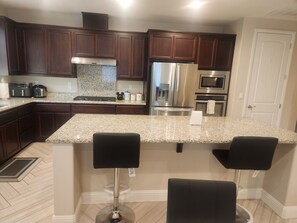 A kitchen with dark wood cabinets, granite countertops, stainless steel appliances, and a bar area with two stools. - Fantastic 4-bedroom house with AC in cool Bay Point (Bay point)