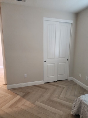 A room with a double door, light-colored walls, and a herringbone-patterned wooden floor.
