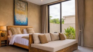 Un dormitorio con cama, sofá, mesita de noche, lámpara, un cuadro y vistas a zonas verdes.