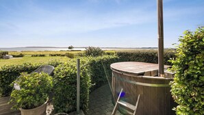 A wooden sauna with a chimney, surrounded by greenery and a view of a body of water. - Stunning Sea Views, Wood-Fired Hot Tub & Nature (Haarby)