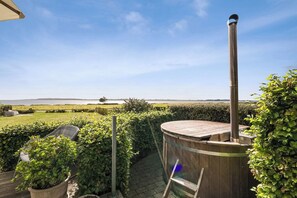 A wooden sauna with a chimney, surrounded by greenery and a view of a body of water. - Stunning Sea Views, Wood-Fired Hot Tub & Nature (Haarby)
