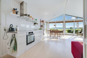 A modern kitchen with an integrated dining area, large windows, and a view of the outdoors. - Stunning Sea Views, Wood-Fired Hot Tub & Nature (Haarby)