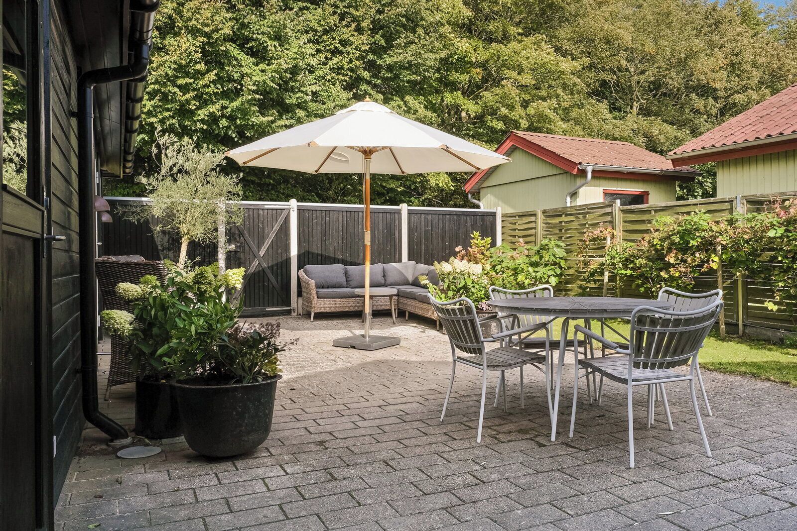 Eine Terrasse im Freien mit Tisch, Stühlen und einer Sitzecke, sowie einem großen Sonnenschirm.