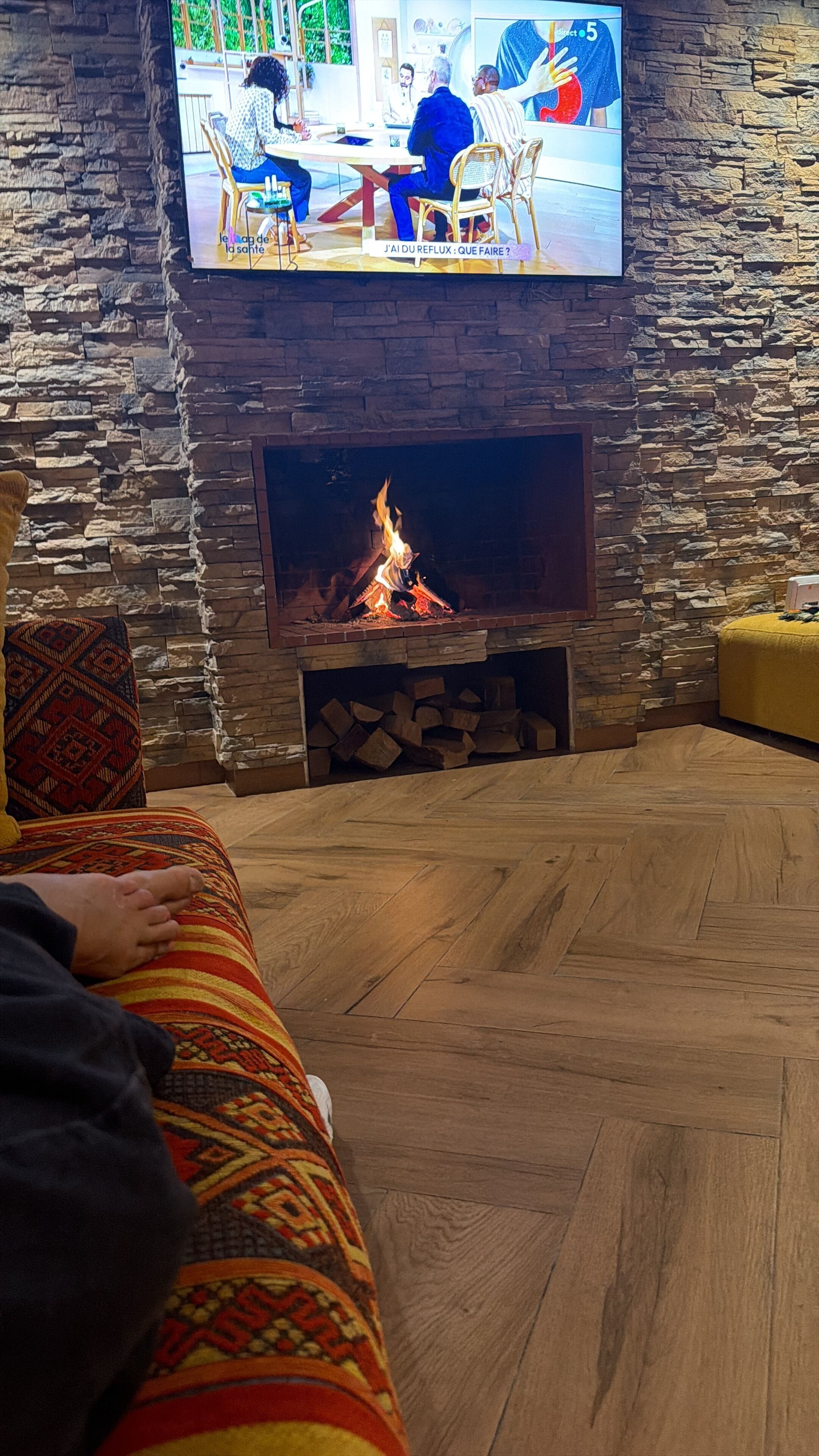 Ein gemütliches Wohnzimmer mit Steinwand, Kamin und darüber montiertem Fernseher.