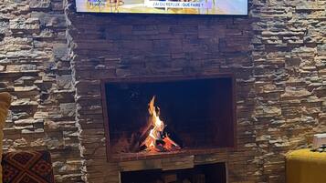 Ein gemütliches Wohnzimmer mit Steinwand, Kamin und darüber montiertem Fernseher.