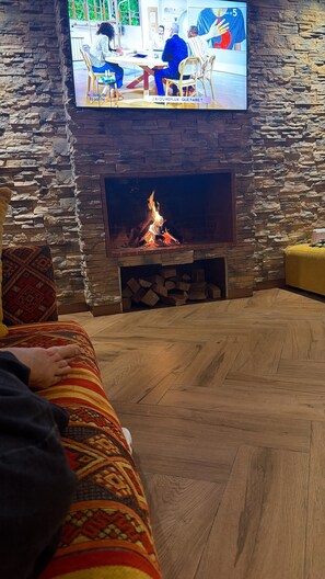 A cozy living room with a stone wall, a fireplace, and a television mounted above it.