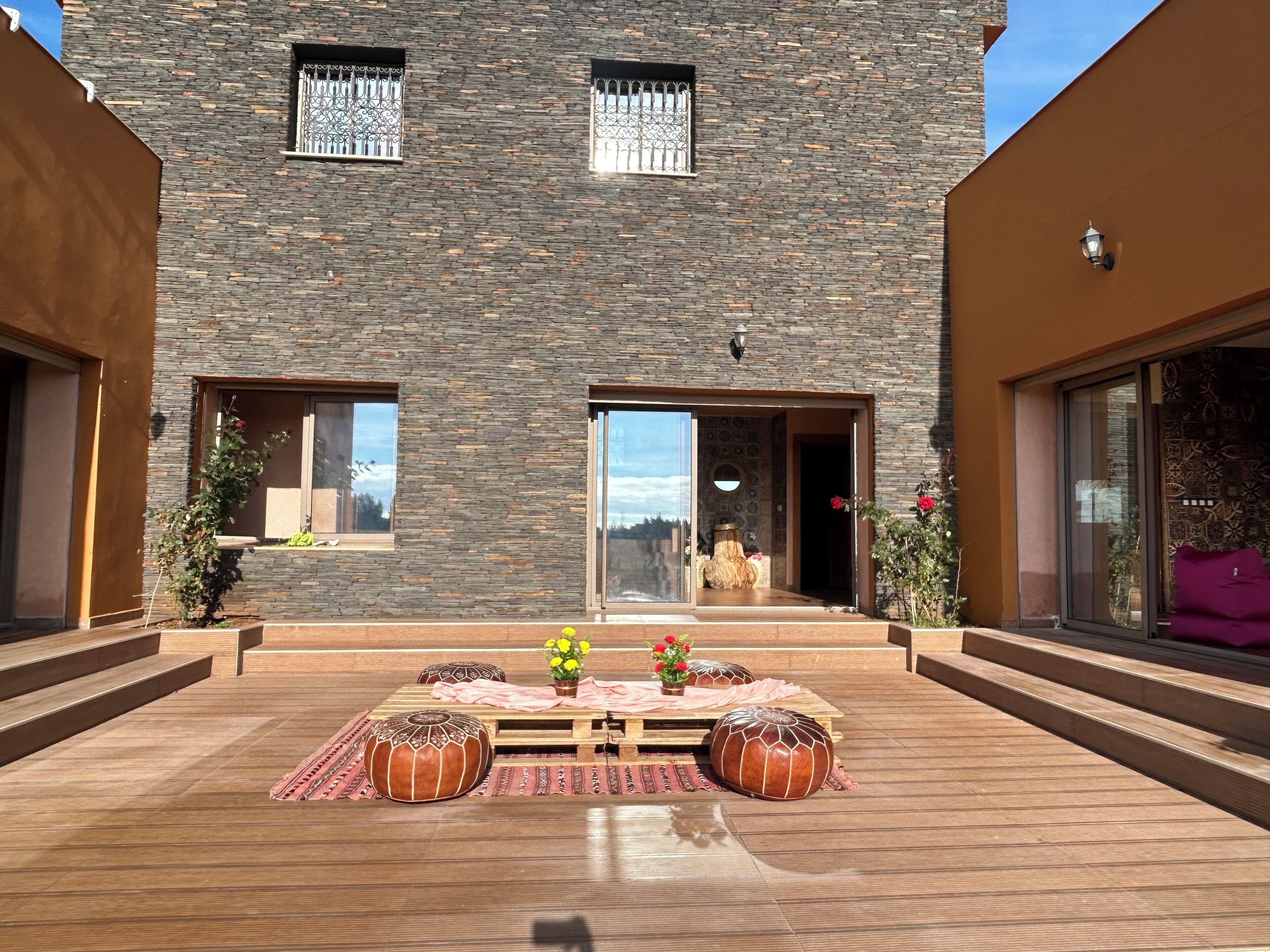Een modern gebouw met een stenen gevel, grote ramen en een houten terras met zitplaatsen.