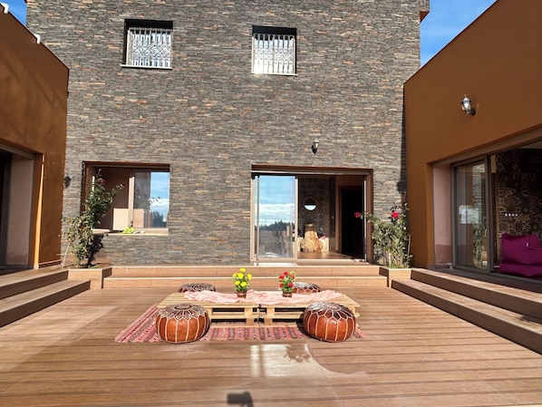 A modern building with a stone facade, large windows, and a wooden deck with seating.