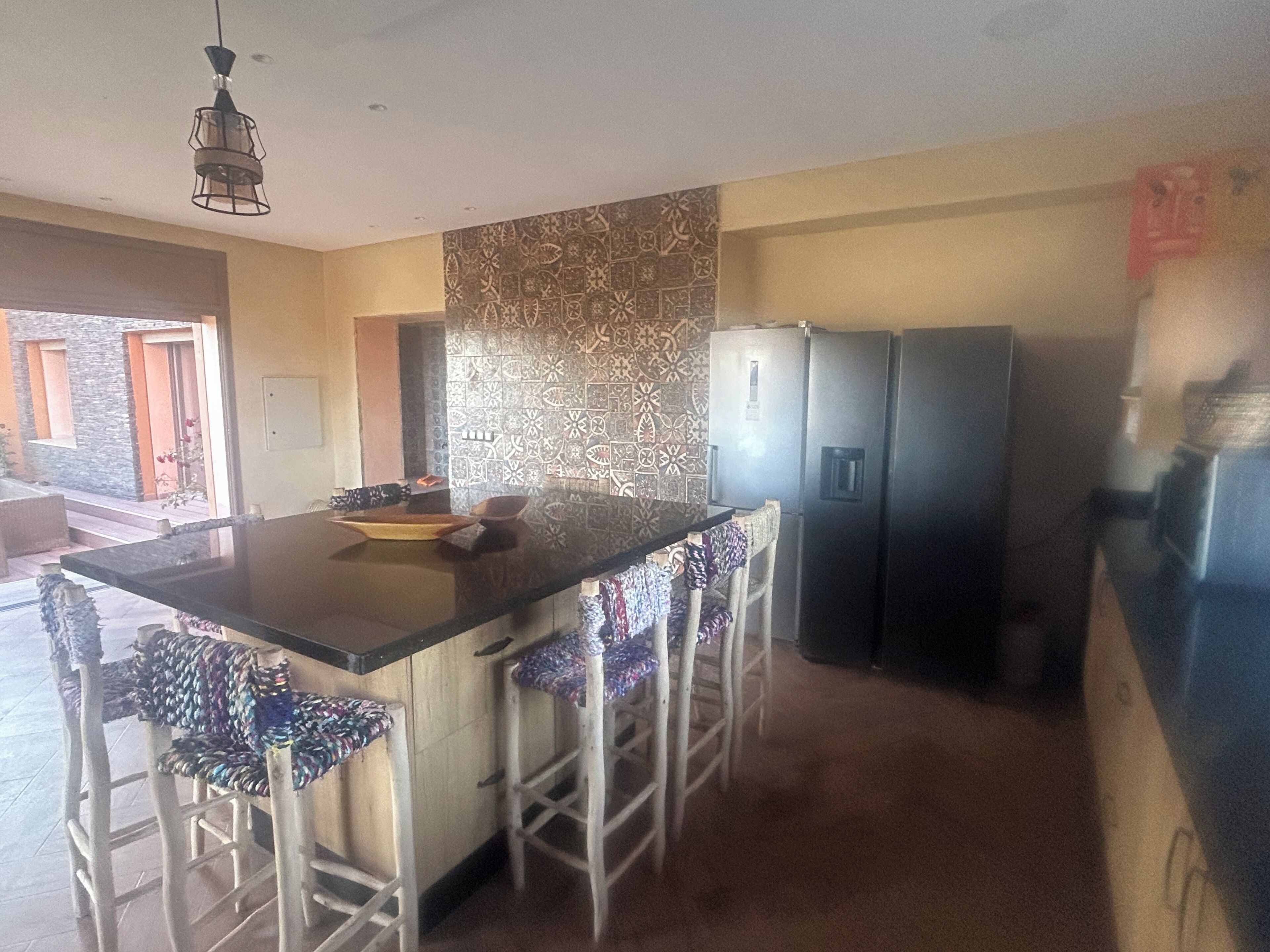 A kitchen with a central island, bar stools, a refrigerator, and a patterned backsplash.