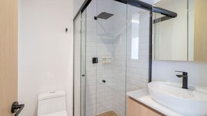 A modern bathroom with a glass-enclosed shower, a white toilet, and a sink with a mirror above it. - Myla - Loft LowF Near Centro Historico (Mexico City)