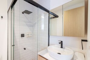 Ein modernes Badezimmer mit einer gläsernen Duschkabine, einem weißen Waschbecken und einem Holzschrank.