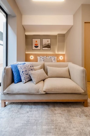 A modern living room with a beige sofa, patterned cushions, and wall-mounted lighting. - Myla - Garden Loft 08 Near Centro Historico (Mexico City)